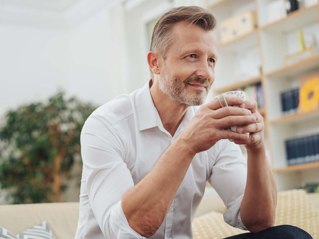 Mann sitzt lächend auf dem Sofa mit einer Tasse in der Hand