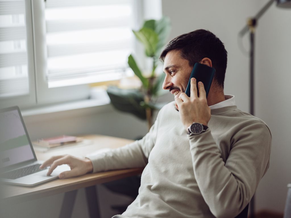 Junger Mann telefoniert am Schreibtisch mit Handy